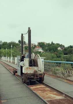 Old rusty mechanical winch mechanism on rails along concrete bridge of Korsun Shevchenkivskyi hydroelectric dam, industrial engineering equipment backdrop.
