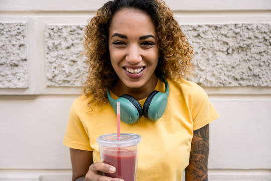 Smiling woman with headphones holding a healthy drink outdoors