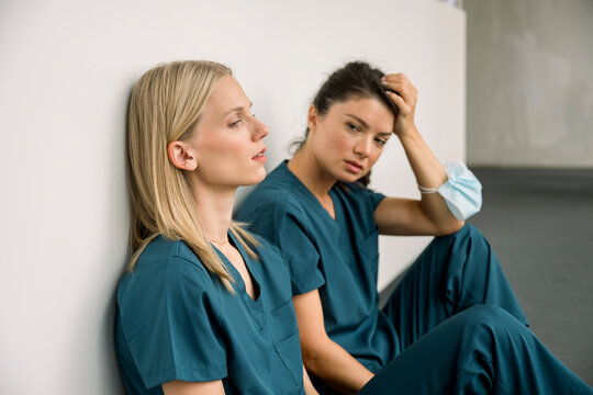 Tired nurses in scrubs sitting indoors at hospital feeling exhausted