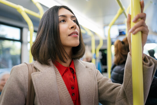 Young woman stands holding a pole on a public bus in the morning