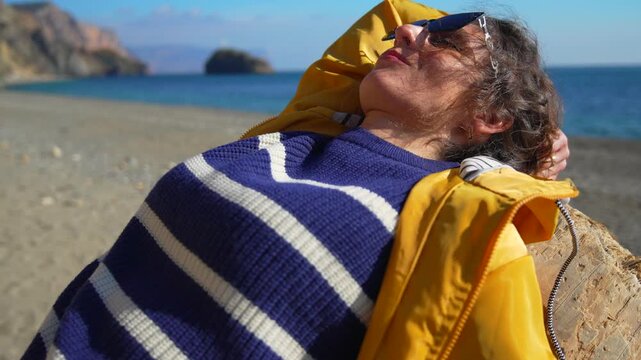 Woman beach relaxation enjoying the warm sun on a sandy shore wearing a yellow jacket and striped sweater for vacation bliss