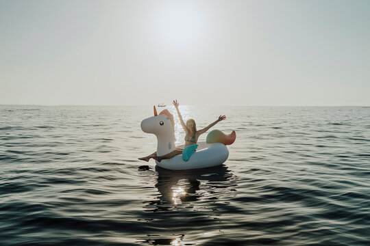 A happy woman enjoys a summer vacation on a unicorn float in the sea