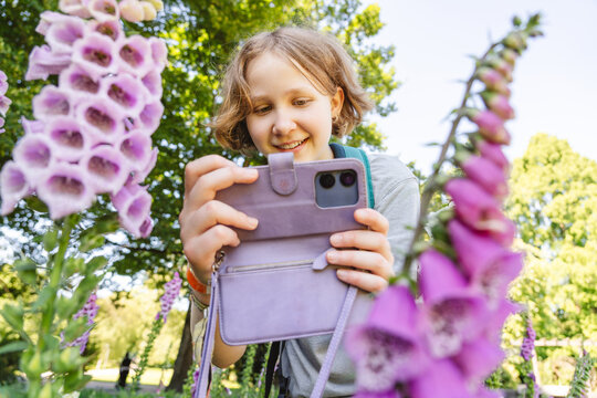 Smiling girl photographs purple foxglove flowers with a smartphone