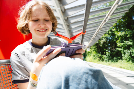 Smiling girl plays mobile game on smartphone at public transport stop