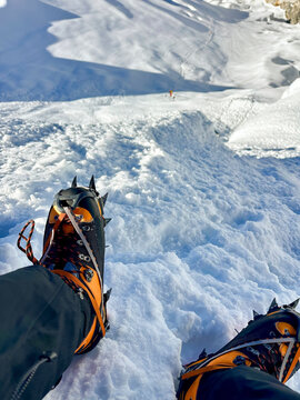 Climber's feet in high-altitude boots and crampons on a snowy slope, first-person view