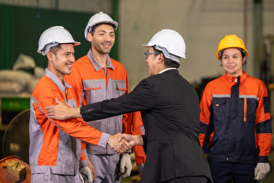 Chief engineer congratulating young engineer with handshake. Outstanding performance recognition during factory team meeting.