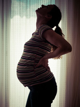 Pregnant woman with back ache against bright window