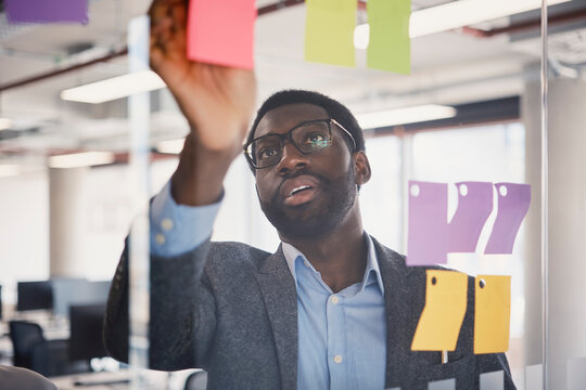 Businessman organizes sticky notes on glass wall at the office