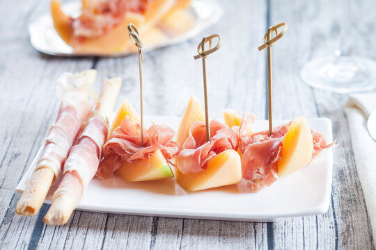 Plate of Charentais melon slices with ham and Grissini wrapped with ham
