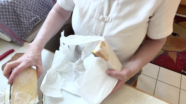 A woman takes several individually wrapped pieces of cheese from a paper shopping bag and places them on the kitchen table while preparing breakfast. High-angle static shot