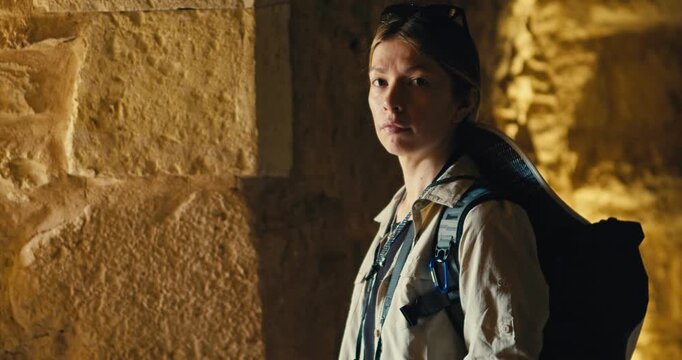 Female tourist with a backpack stands inside the historic stone interior of Ajloun Castle, Jordan, looking toward the camera in warm natural light while exploring the medieval fortress