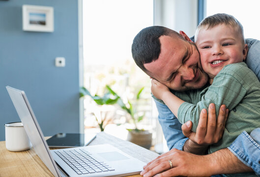 Father and son hug at home while working on a notebook