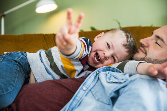 A smiling son enjoys fun time with his father on the couch at home