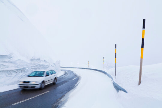 A blurred car navigates a snowy mountain pass in Switzerland