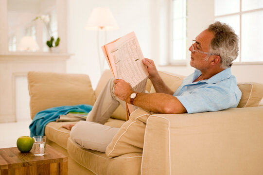 Mature man reading newspaper on sofa, side view