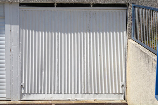 A front view of a closed white corrugated metal garage door with vertical patterns under direct sunlight.