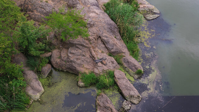 Top view of granite rocky river bank with green trees and duckweed water on Ros river in Korsun-Shevchenkivskyi, natural outdoor landscape backdrop for nature travel project.