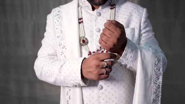 Indian groom in traditional white sherwani adjusting cuff for wedding ceremony