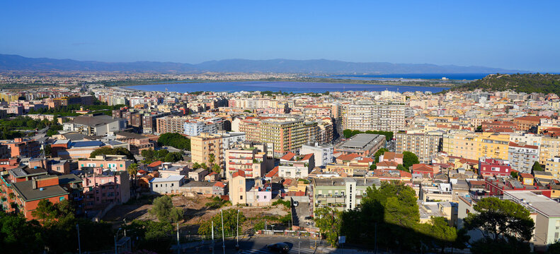 Aerial view over the rooftops of Cagliari towards the Molentargius-Saline Regional Natural Park lagoon and mountains, Sardinia, Italy
