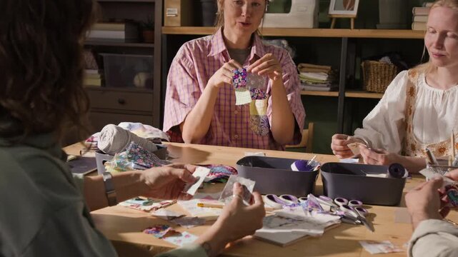 Caucasian woman explaining patchwork technique to group of Caucasian women during creative workshop, camera tilting down. Clip is ideal for promoting craft classes or hobby schools