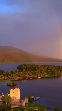 Vertical drone video: flying towards a rainbow over Ross castle and Killarney lake in County Kerry, Ireland, Irish travel route of Ring of Kerry, Irish nature, aerial sunrise view of Killarney