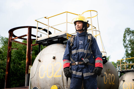 Firefighter wearing protective gear and breathing apparatus stands beside industrial tanks