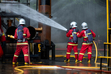 Naklejka premium Firefighters use water hoses to control flames during a coordinated industrial fire