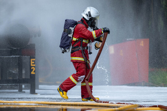 Firefighter wearing full protective equipment operates a water hose
