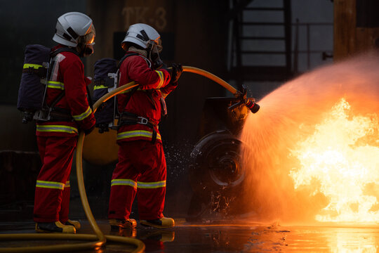 Firefighters in protective gear spray water to extinguish flames