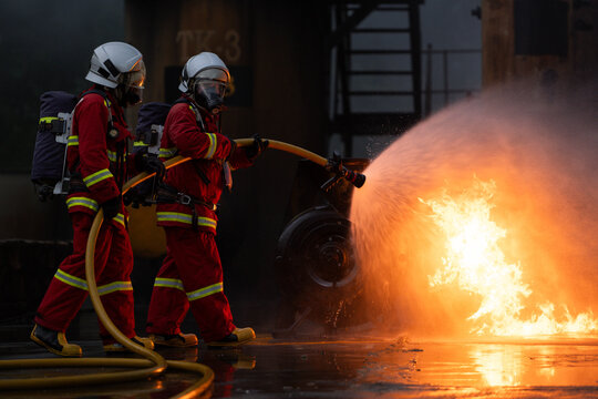 Firefighters in protective gear spray water to extinguish flames