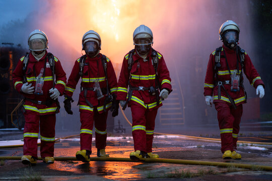 The four firefighters in protective gear walk through the remaining smoke and flames