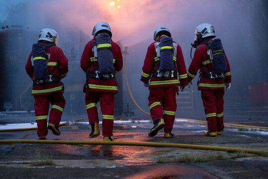 The four firefighters in protective gear walk through the remaining smoke and flames