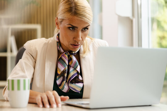 Woman Working in a Small Office With a Laptop and a Cup of Coffee During the Day