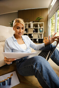 Woman Working in Small Office at Home While Reviewing Documents and Using Laptop