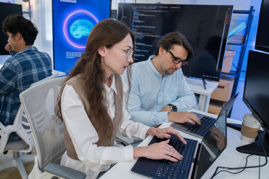 Caucasian woman and man working side-by-side on laptops with AI technology background graphics.