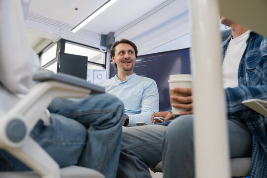 Low angle shot of Caucasian manager holding coffee cup while conversing with colleagues in office.