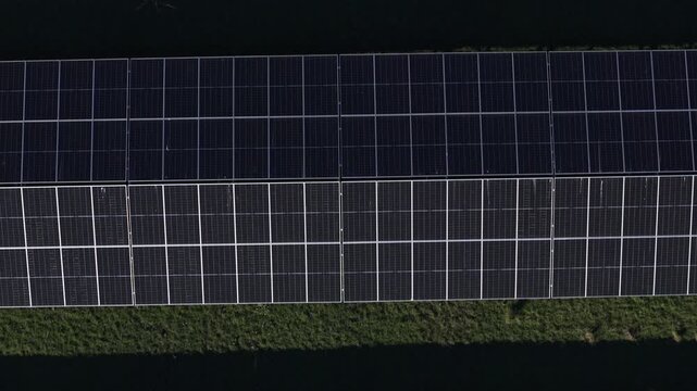 Cinematic aerial footage of expansive solar panels in The Basin, Melbourne. Clean energy, geometric patterns, sharp sunlight, and green grass create a modern, sustainable landscape. Aerial footage.
