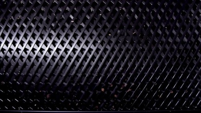 Dark metallic mesh illuminated by moving studio light creates a modern industrial texture background.