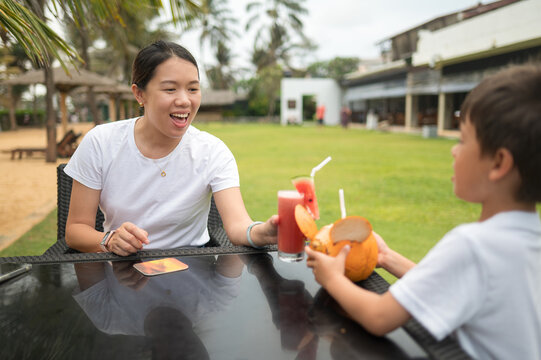 Woman shares refreshing drinks with young boy at outdoor restaurant in Sri Lanka