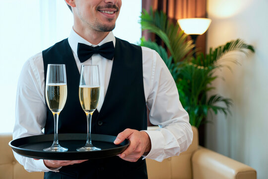 Caucasian young adult waiter carrying tray with champagne flutes during hospitality service, representing premium catering. Useful for restaurant marketing, event promotion