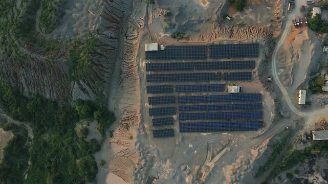 Rows of renewable solar energy panels powering a massive open pit gravel mining operation surrounded by deeply eroded earthworks and trucks in Punjab Pakistan