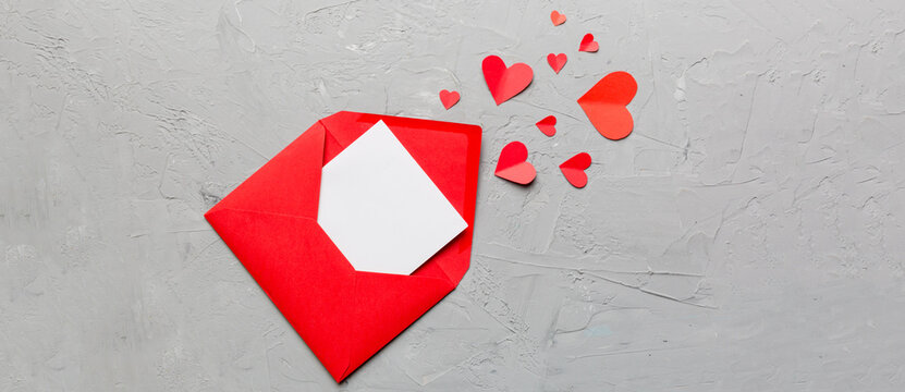 Red paper envelope with empty white card and heart on colored background. top view valentines day concept