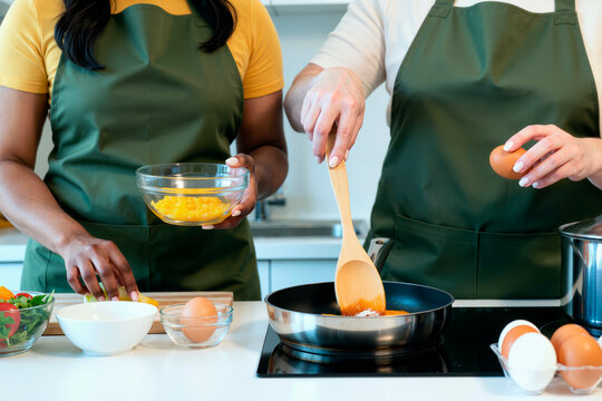 Cropped multiethnic women preparing meal together, stirring pan and adding ingredients in kitchen, showing teamwork and home cooking. Ideal for food blog, cooking class, healthy eating