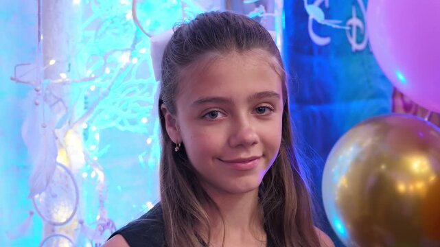Charming young girl with sweet smile posing in dreamy room decorated with whimsical dreamcatcher and glowing purple light against white brick wall
