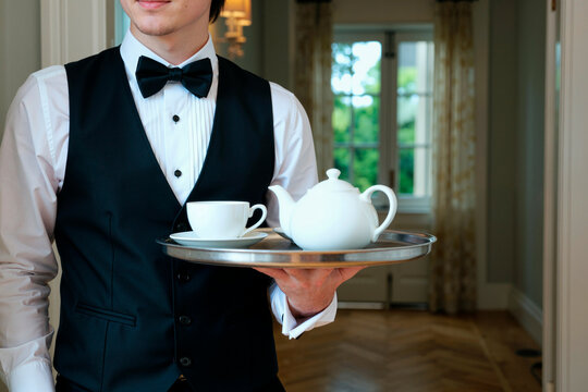 Young adult man serving tea on tray in formal hospitality setting, presenting catering and premium service concept. Useful for hotel marketing, event service, luxury dining promotion