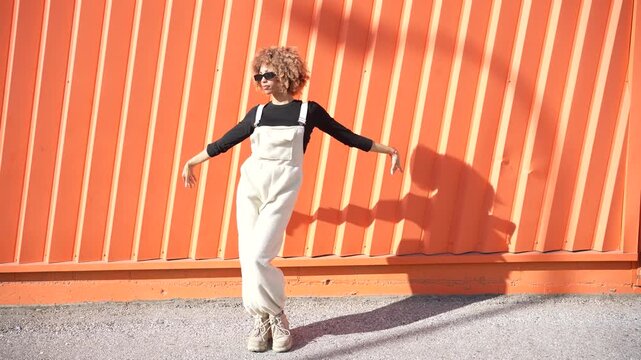 A stylish model poses confidently against a vibrant orange wall, showcasing her outfit