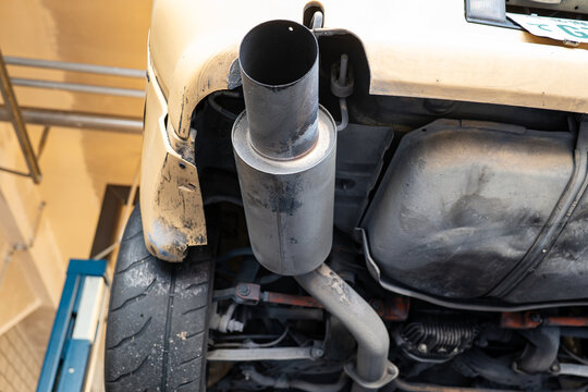 Low angle close up view of a large single cannon exhaust tip, rear silencer, and underbody components on a raised vehicle.