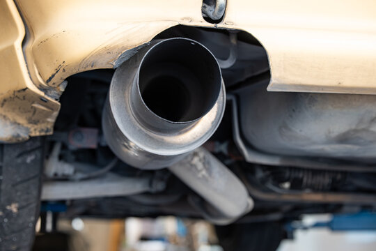 Low angle close up view inside a wide cannon exhaust tailpipe tip and rear muffler box on a vehicle elevated on a workshop lift.
