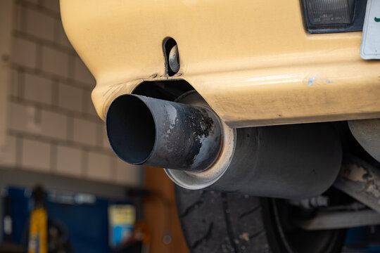 Low angle close up view of a large soot-stained cannon exhaust tip and rear bumper cut-out on a vehicle raised on a lift.