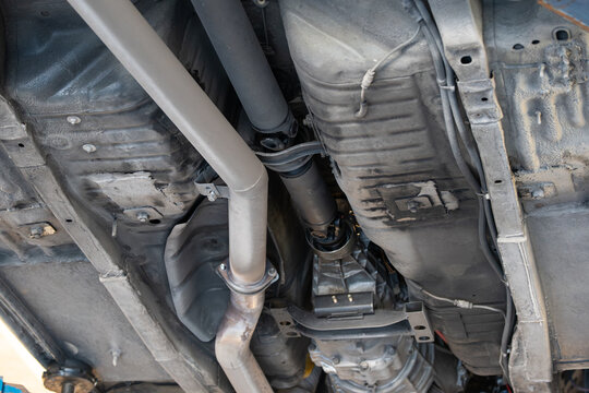Low angle view from below detailing the central driveshaft, transmission rear mount, exhaust pipe, and chassis floor pan.